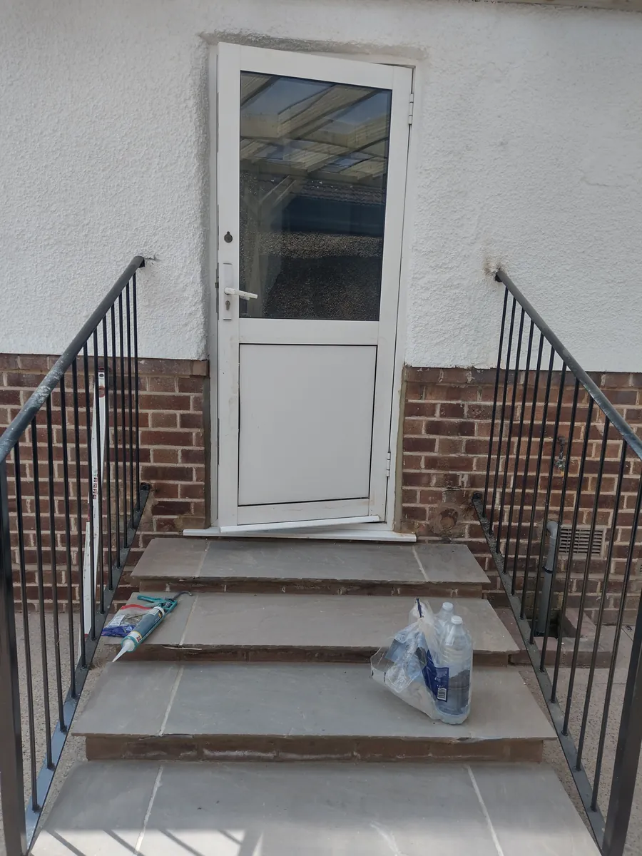 White door with paved steps and metal railings against a rendered and brick wall