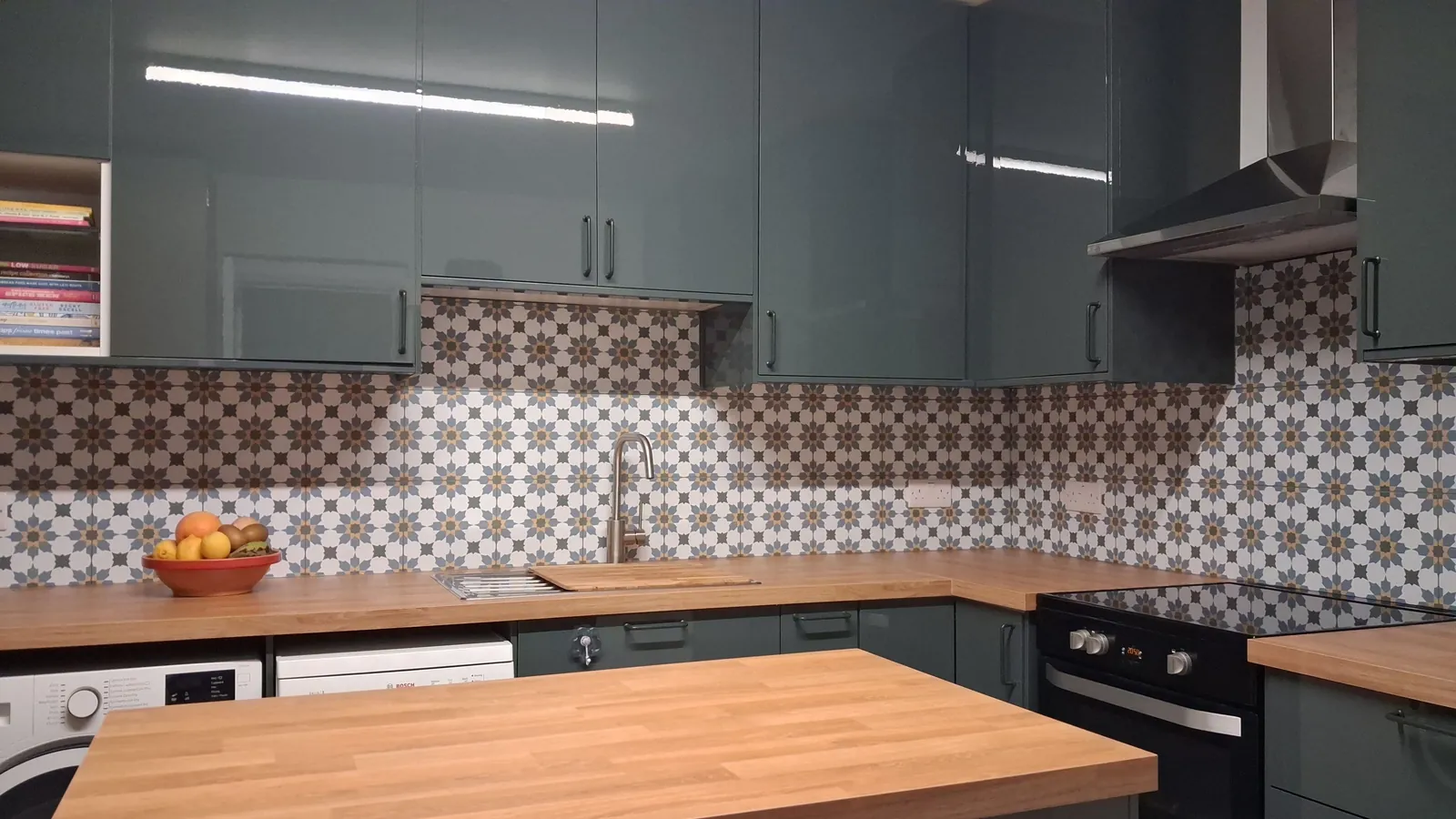 A fitted kitchen with green gloss units, oak-effect worktops and a patterned tiled splashback