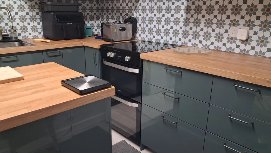 Fitted kitchen with green units, oak-effect worktops and a patterned tiled splashback