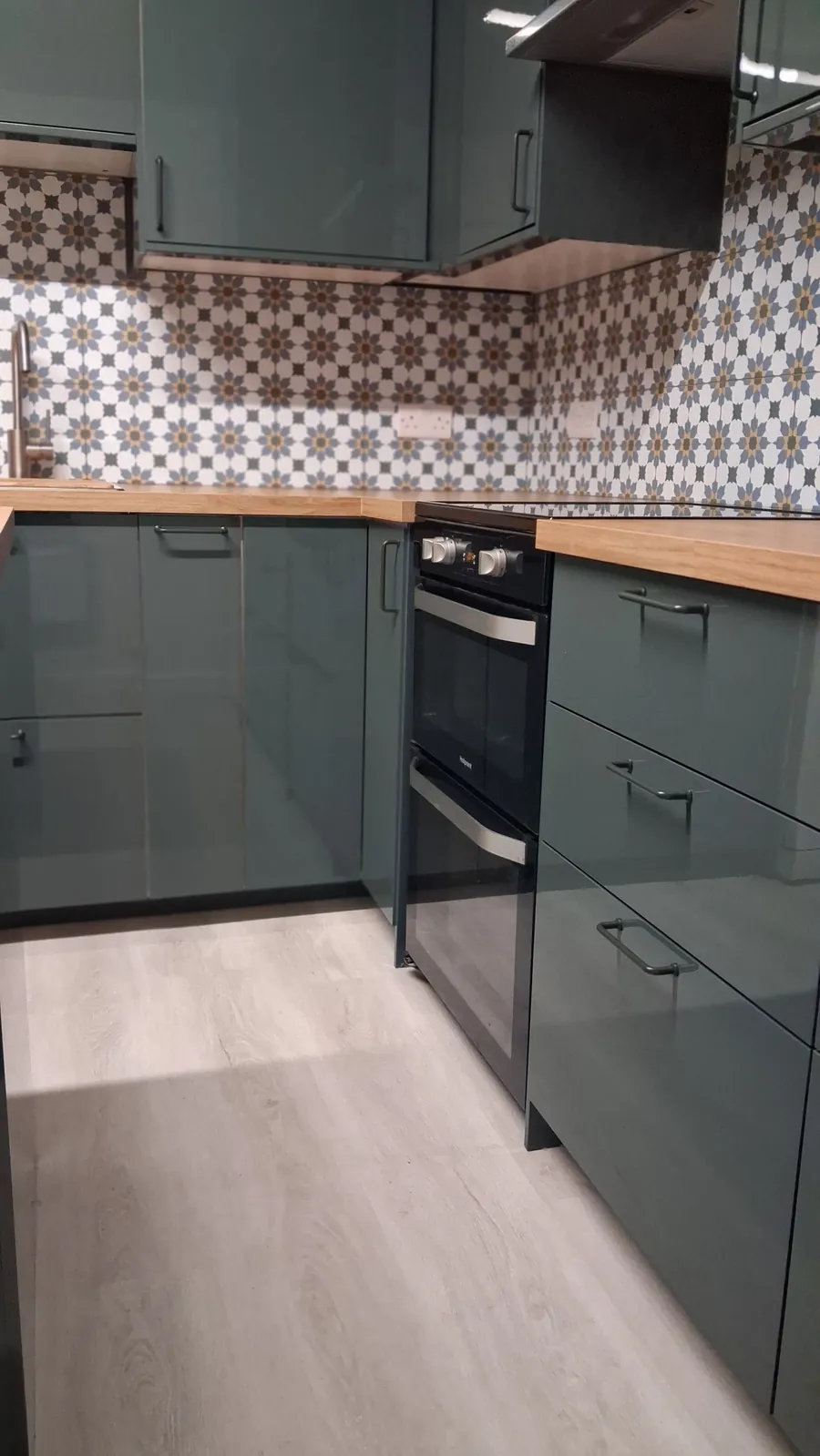 Green kitchen units, built-in oven and patterned tiles