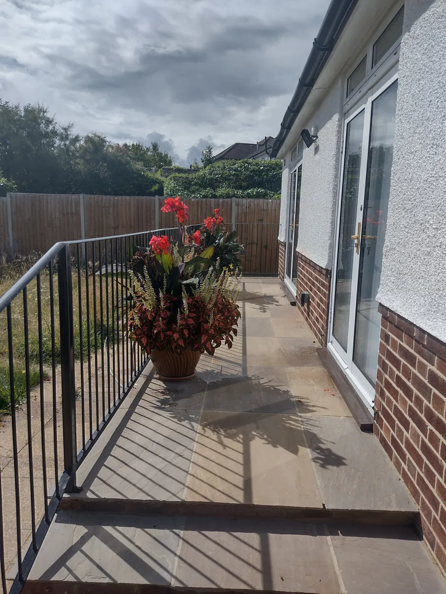 Paved patio beside a brick and rendered extension with black metal railings
